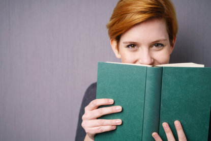 lachende frau versteckt sich hinter einem buch - 