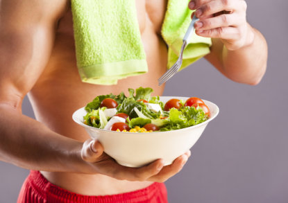 Fit man holding a bowl of fresh salad on grey background - 